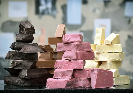 Dark, milk, ruby and gold chocolate pieces stacked on a table.